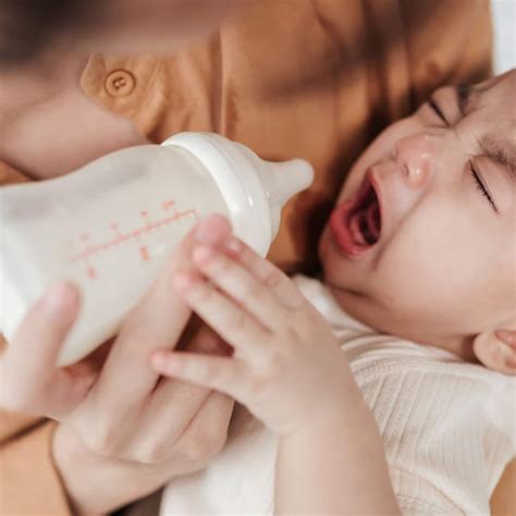 Illustratie van een baby die een fles weigert, met een gefrustreerde ouder ernaast.