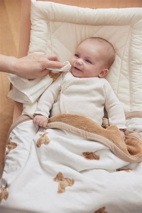 Een baby die comfortabel slaapt onder een Jollein Teddy Bear deken in een wiegje.