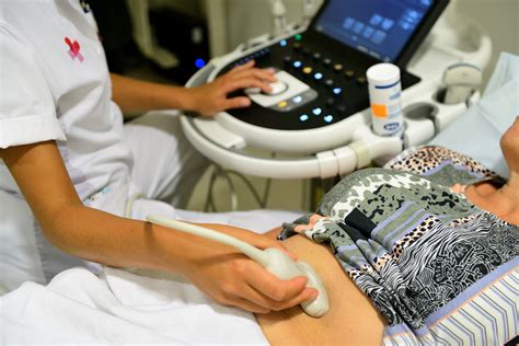 Een afbeelding van een echoscopist die een echo uitvoert op de buik van een zwangere vrouw, met een monitor die het beeld van de baby toont.