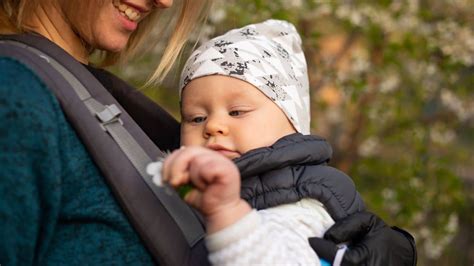 Een man die een baby draagt in een draagzak, met een thermosbeker in de hand.