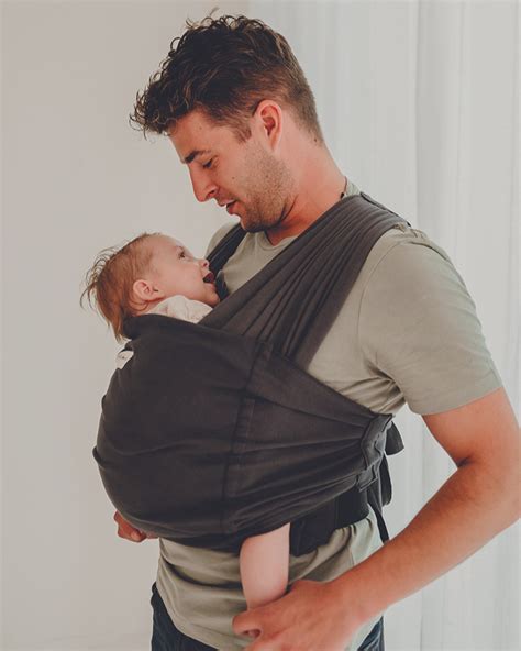 Foto van een ouder die een baby in een draagdoek op de buik draagt, met de baby alert en de omgeving observerend.