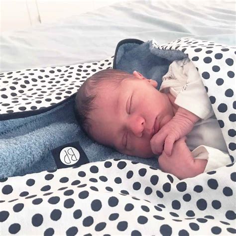 Een zachtroze baby wikkeldoek met een capuchon, waar een naam op geborduurd is.