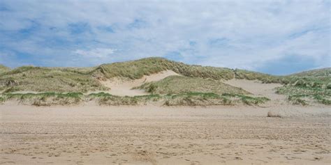 Luchtfoto van een breed Nederlands zandstrand met duinen en badgasten.