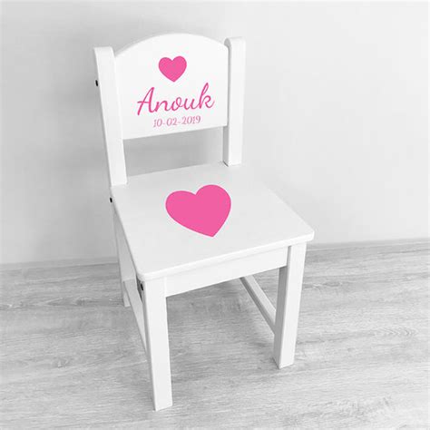 Een houten geboortestoeltje met de naam van een baby erop gegraveerd, naast een bosje bloemen.