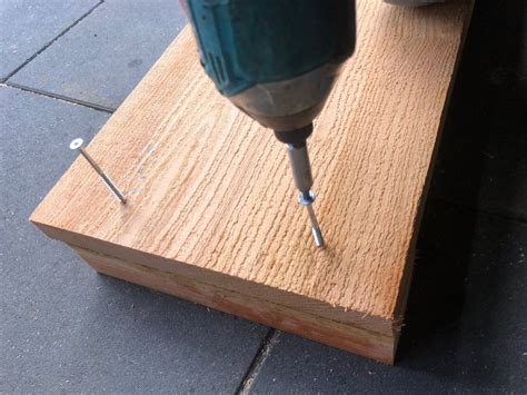 Een persoon die met schroeven een houten geboortebord aan een paal bevestigt.