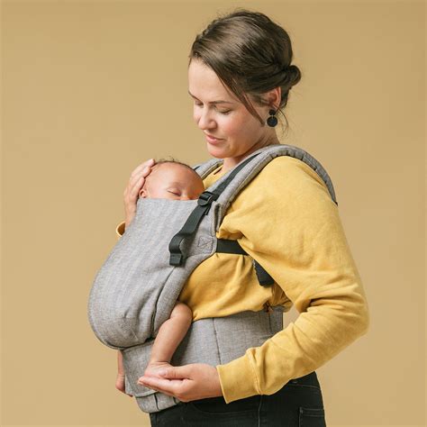 Een ouder die een baby met het gezicht naar voren draagt in een ergonomische draagzak.
