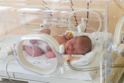 Afbeelding van een baby in een couveuse met medische apparatuur.