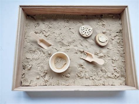 Foto van een sensorische speelbak gevuld met kinetisch zand en diverse hulptools.