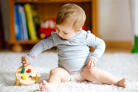 Baby die op zijn buik ligt en speelt met speelgoed, met de bedoeling om de motorische ontwikkeling te stimuleren.