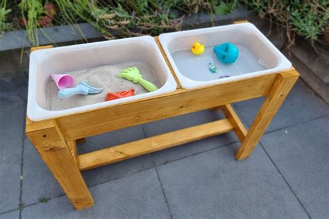 Een kind dat vrolijk speelt met een zand- en watertafel, inclusief diverse zandschepjes en vormpjes.