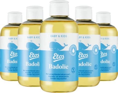 Een baby die in bad wordt gehouden, met een flesje badolie op de achtergrond