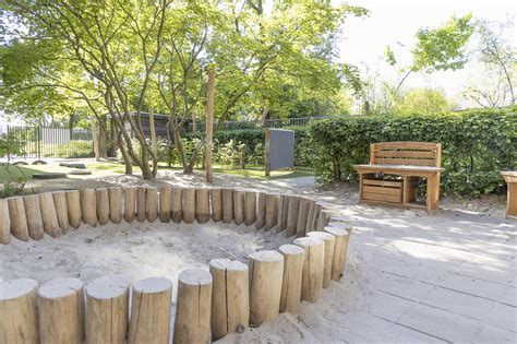 Foto van de groene tuin van Kindergarden Arnhem Elderveld met diverse speelelementen en veel bomen.